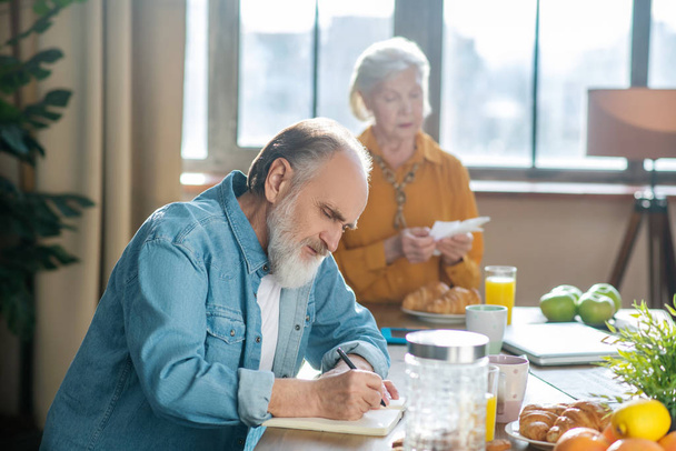 Bearded grey-haired man sitting at the table and making notes - Photo, Image