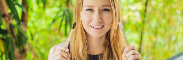 Young woman holds a bamboo toothbrush on a background of green growing bamboo BANNER, LONG FORMAT - Foto, Imagem
