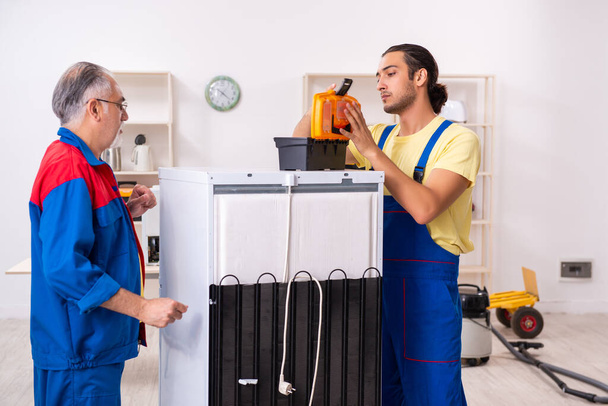 Dois empreiteiros reparando geladeira na oficina
 - Foto, Imagem
