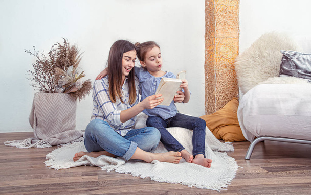 Mom reads a book with her cute daughter at home. Children's development and education, family values. The concept of children's friendship and family . - Foto, Imagen