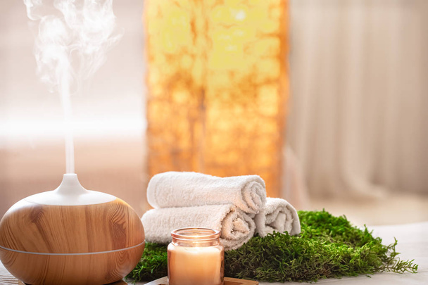 Spa composition with the aroma of a modern oil diffuser with body care products . Twisted white towels, spring greens and flowers. Spa concept for body and health care . - Photo, Image