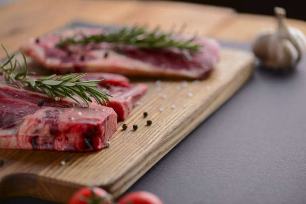 Fresh raw steak on wooden cutting board over black background with spices, top view. - 写真・画像