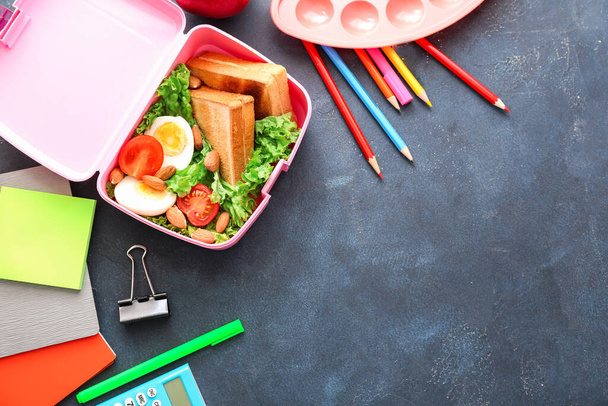 Шкільна обідня коробка зі смачною їжею та канцелярськими товарами на столі
 - Фото, зображення
