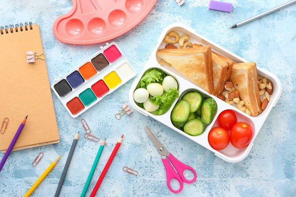 School lunch box with tasty food and stationery on table - Valokuva, kuva