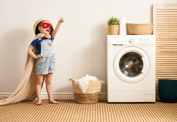 Beautiful child girl little helper is having fun and playing while doing laundry at home.    - Fotó, kép