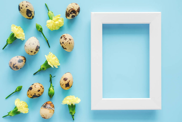 Spring yellow flowers, organic natural quail eggs and white frame on blue background. Happy Easter and zero waste concept. Copy space, mock up. Creative Flat lay Top view. - 写真・画像