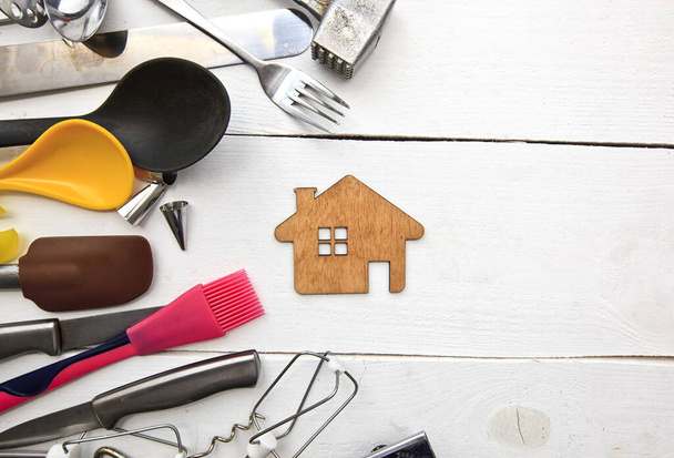 Un sacco di utensili da cucina diversi sul tavolo di legno e una piccola casa di legno tra di loro
 - Foto, immagini