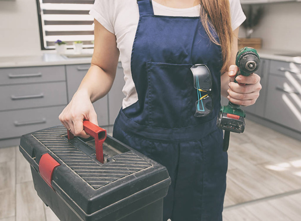 La femme réparatrice habillée en uniforme de travail dans la maison avec boîte à outils et d'autres équipements à la main
 - Photo, image