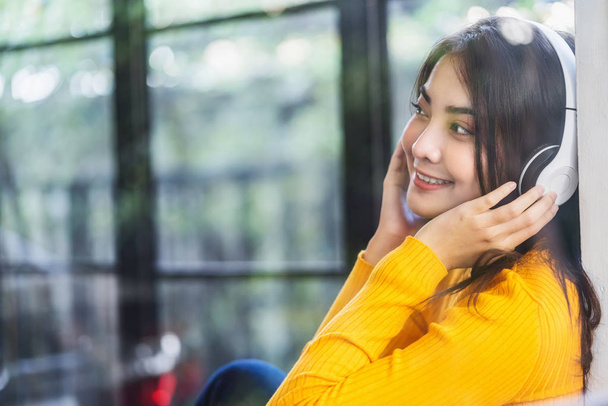 Felicidad Mujer joven asiática sonriente que usa auriculares inalámbricos de tecnología para escuchar la música a través de un teléfono móvil inteligente en una cafetería o espacio de coworking, estilo de vida y ocio con concepto de hobby
 - Foto, imagen