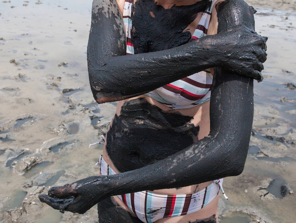 Donna che diffonde fango nero curativo sul suo corpo. Primo piano. - Foto, immagini
