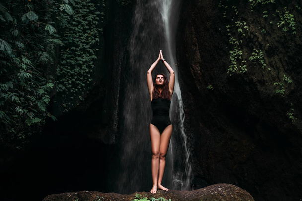 A woman does yoga at a waterfall. Healthy lifestyle. The concentration of the body. A woman does yoga in Bali. A woman meditates in nature. Meditation at the waterfall. Young woman practicing yoga - Foto, immagini
