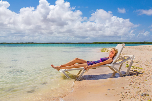 Λευκή γυναίκα κάνει ηλιοθεραπεία στο βυθό της παραλίας δίπλα στη θάλασσα στο Bonaire - Φωτογραφία, εικόνα