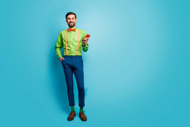 Full length body size view of his he nice attractive cheerful cheery guy wearing cool funky festal look using cell isolated over bright vivid shine vibrant blue green teal turquoise color background - Foto, afbeelding