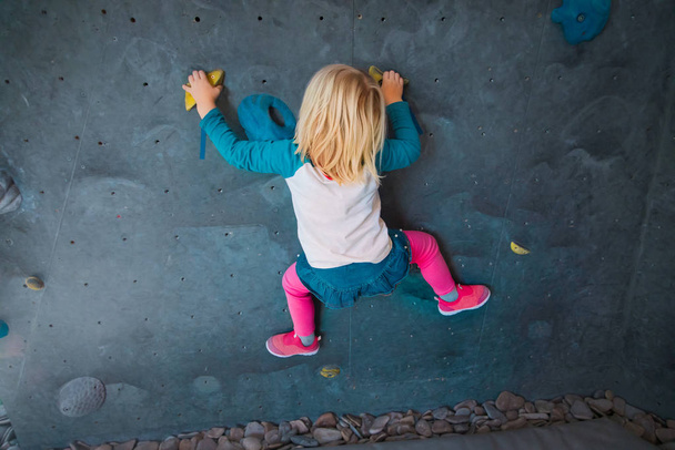 Spor salonunda küçük bir kız yapay kaya duvarına tırmanıyor. - Fotoğraf, Görsel