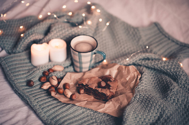 Téli koncepció. Egy csésze forró kávé csokis pitével mogyoróval és égő gyertyákkal karácsonyi fények mellett. Téli ünnepek. Jó reggelt..  - Fotó, kép