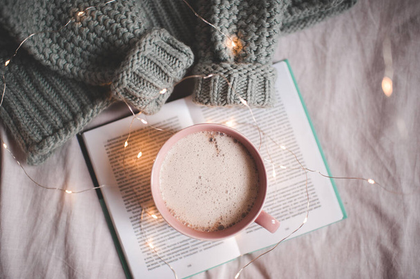 Cup of coffee with oprn book and knitted wool sweater in bed closeup. Top view. Autumn season. - Foto, Imagen