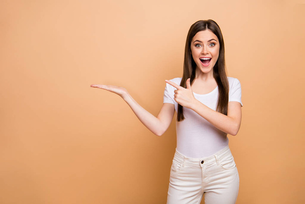 Portrait of astonished crazy girl hold hand point index finger recommend adverts suggest select promo wear white pants trousers isolated over beige color background - Photo, image