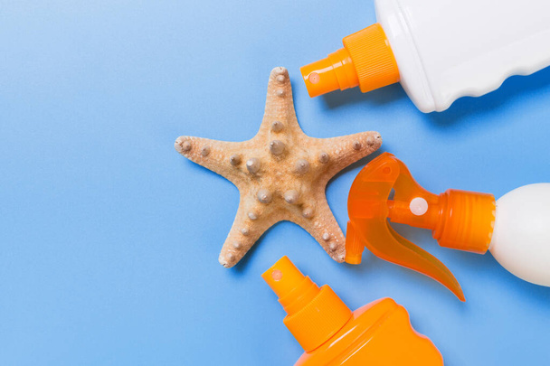 sunscreen cream with starfish and seashells in bottles on blue background, top view. - Foto, Imagem