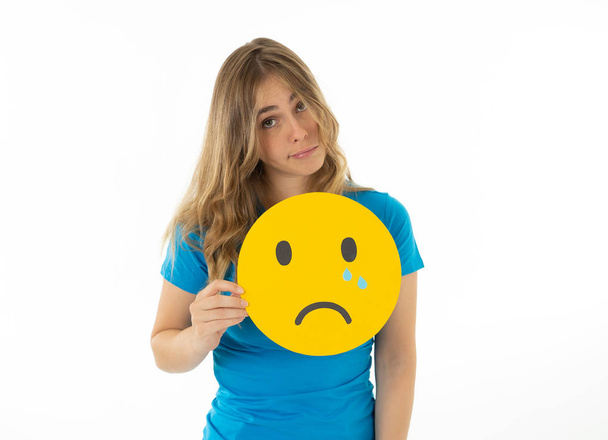 Young woman holding sad crying face emoticon icon feeling unhappy about news in social media on the internet. Facial expressions, social network, notification icons and technology concept. - Fotó, kép
