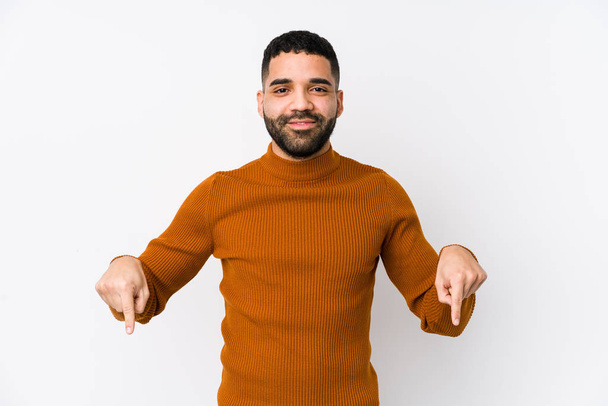 Young latin man against a white background isolated points down with fingers, positive feeling. - Foto, imagen
