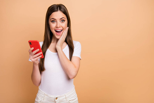 Portrait of astonished excited girl use cellphone enjoy social network notification read impressed scream wow omg wear white casual style outfit isolated over beige color background - Foto, imagen