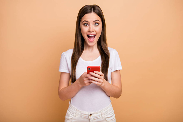 Portrait astonished cheerful girl use smartphone get incredible social network notification impressed scream unbelievable unexpected wear good look outfit isolated beige color background - Foto, imagen