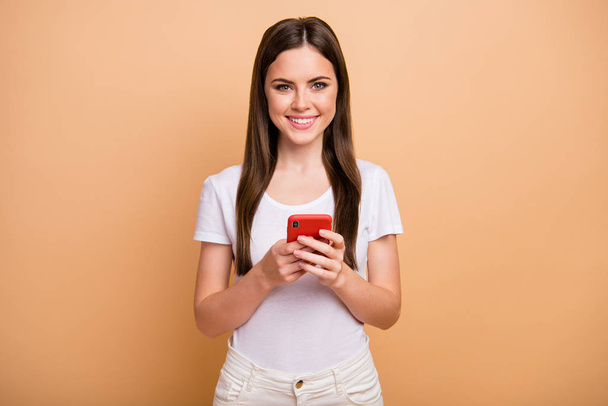 Portrait of positive cheerful girl social network user use cell phone enjoy chatting with her blog followers wear modern clothing isolated over beige color background - Фото, изображение