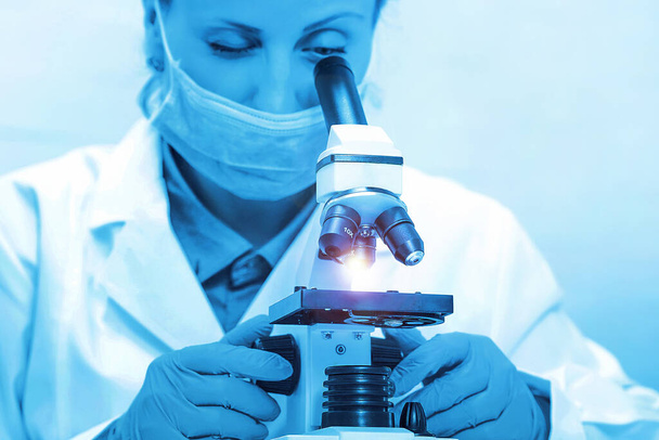 Laboratory microscope. Scientist with a microscope studying samples and liquid. Medical research with technical equipment. Woman student with microscope in the laboratory on blue background. - Photo, Image