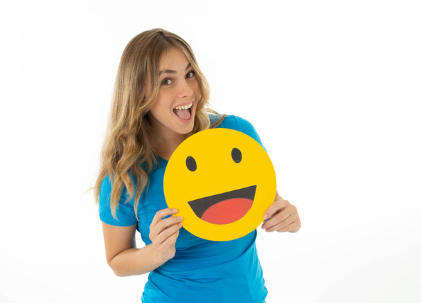 Attractive young woman holding happy face emoticon icon excited to be liked in social media in facial expressions, social network, notification icons and technology communication. - Fotó, kép