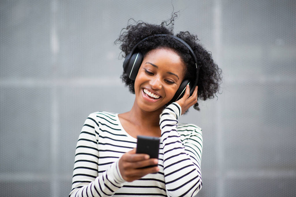 Портрет счастливая молодая африканская женщина слушает музыку с мобильного телефона и наушников
 - Фото, изображение