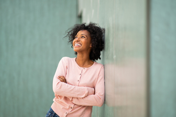 Retrato feliz joven mujer negra apoyada contra la pared verde con los brazos cruzados
 - Foto, Imagen