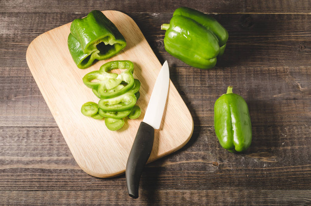 green paprika cut on a wooden board/Slicing peppers on a wooden cutting board with knife on a dark wooden table. Top view - Fotoğraf, Görsel
