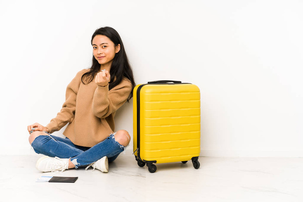 Joven viajera china sentada en el suelo con una maleta aislada señalándote con el dedo como si invitaras a acercarte
. - Foto, Imagen