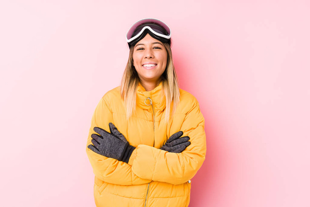若い白人女性がピンクの背景にスキー服を着て笑って楽しい. - 写真・画像