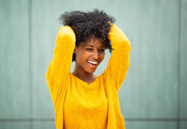 Portrait belle jeune femme afro-américaine souriant avec les mains dans les cheveux par fond vert
 - Photo, image