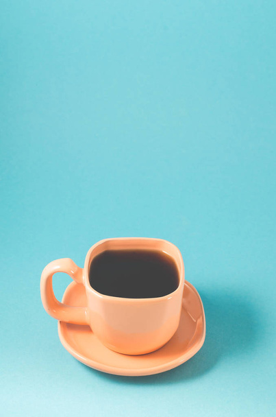 orange cup coffee on a blue background/orange cup with a saucer full of black coffee on a blue background - Foto, imagen