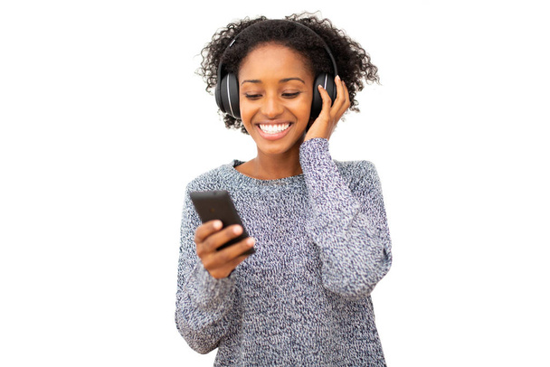 Portrait smiling young black woman with mobile phone and headphones listening to music  against isolated white background - 写真・画像