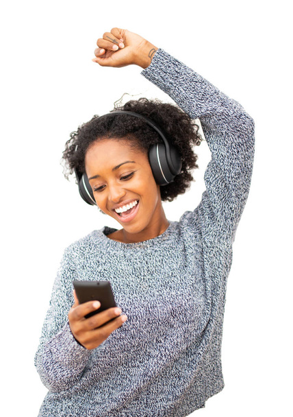 Porträt einer tanzenden jungen schwarzen Frau mit Handy und Kopfhörer, die vor isoliertem weißen Hintergrund Musik hört - Foto, Bild