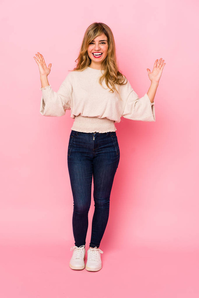 Young blonde caucasian woman standing over a pink background receiving a pleasant surprise, excited and raising hands. - Foto, Imagem