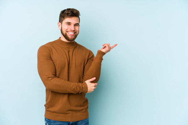 Young caucasian man isolated on blue background smiling cheerfully pointing with forefinger away. - Photo, Image