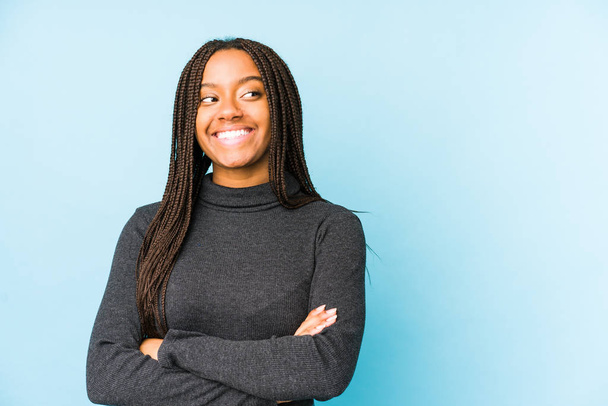 Νεαρή Αφροαμερικανή, απομονωμένη σε μπλε φόντο χαμογελαστή, με σταυρωμένα χέρια.. - Φωτογραφία, εικόνα