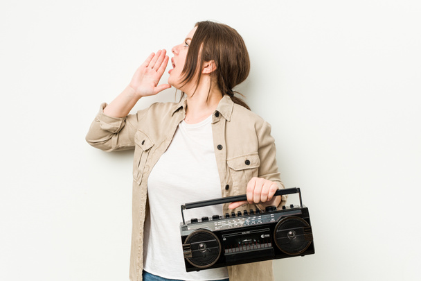 Young curvy woman holding a retro radio shouting and holding palm near opened mouth. - Photo, Image