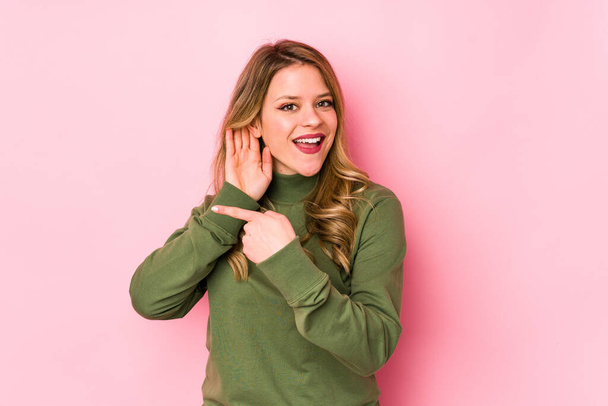 Young caucasian woman isolated on pink background trying to listening a gossip. - Photo, Image