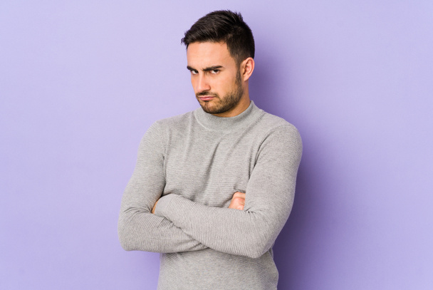 Young caucasian man isolated on purple background frowning face in displeasure, keeps arms folded. - Photo, Image