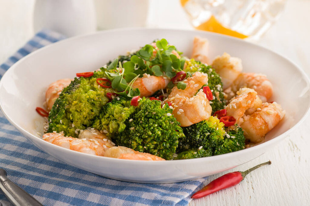 Warm salad with grilled prawns, broccoli, fresh herbs, sesame seeds and chili peppers. Large portion on a white plate. Healthy eating concept. Ready to eat. - 写真・画像