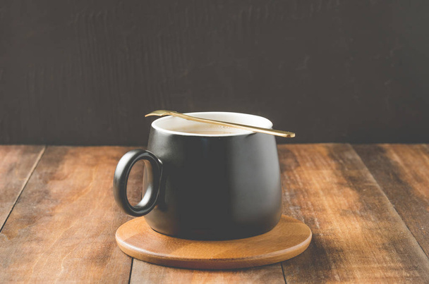 black mug of a cappuccino in a wooden support, on a wooden table - Fotografie, Obrázek