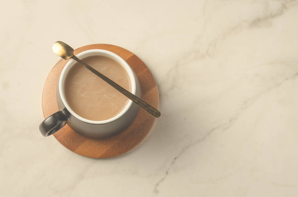czarny kubek cappuccino z łyżką w drewnianym wsporniku, na białym stole. Widok z góry i przestrzeń kopiowania - Zdjęcie, obraz