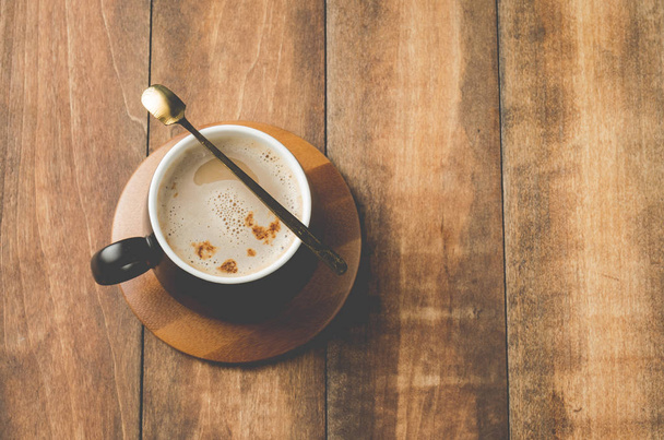 black mug of a cappuccino in a wooden support, on a wooden table, top view and copy space - Fotó, kép