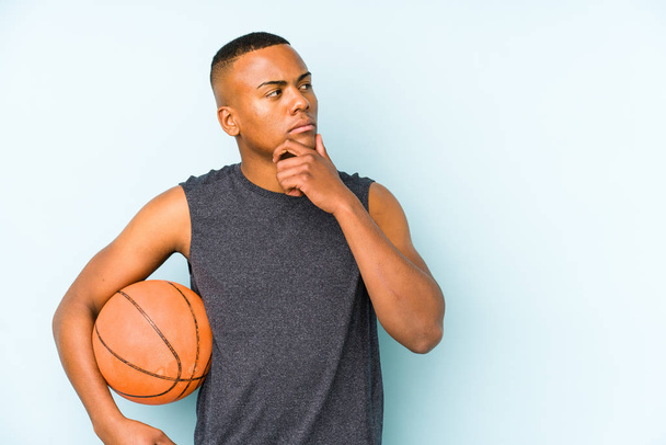 Mladý kolumbijský muž hraje basketbal izolovaně a dívá se stranou s pochybným a skeptickým výrazem. - Fotografie, Obrázek