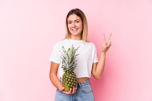 jonge blanke vrouw met een ananas waarop nummer twee met vingers. - Foto, afbeelding